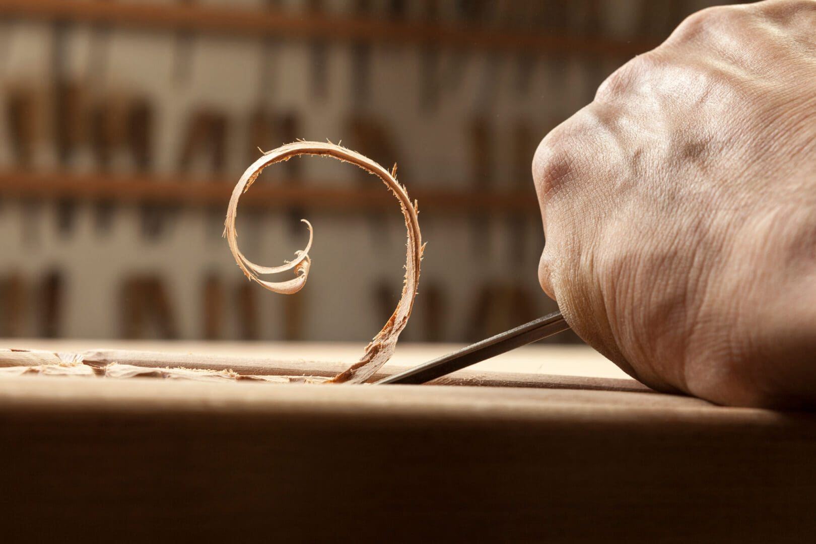 Close-up of a hand carving a wooden curl with a chisel.